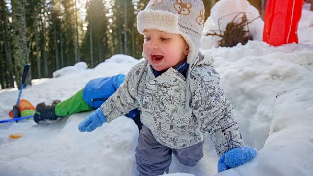 SLO MO蹒跚学步的孩子和他的兄弟在雪中滚动视频素材
