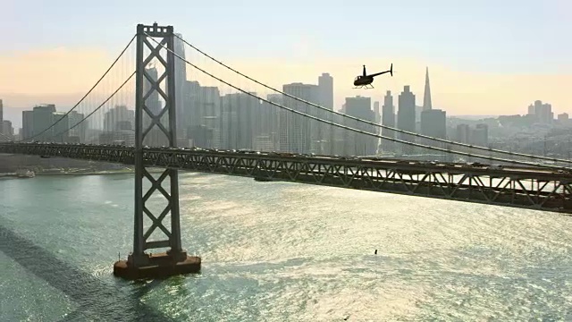 直升飞机沿着旧金山-奥克兰海湾大桥飞行，在背景中俯瞰旧金山市中心视频素材