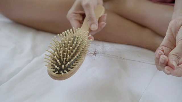 女人的手拉着她的头发从梳子上掉下来，用木梳梳完头发后。视频下载