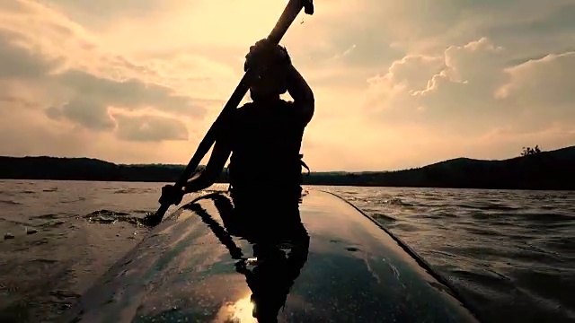 日落时分，女子在平静的湖面上划皮艇视频下载