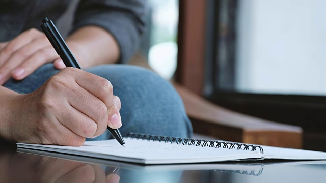 一个女人的手正在桌上一个白纸本上写着什么视频素材