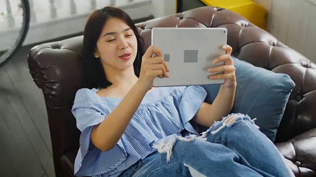 年轻的亚洲美女在家里使用数码平板电脑视频下载