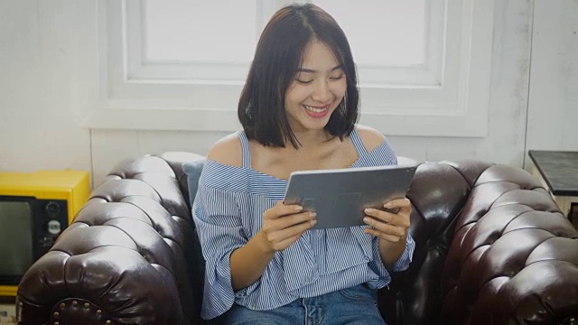 年轻的亚洲美女在家里使用数码平板电脑视频下载