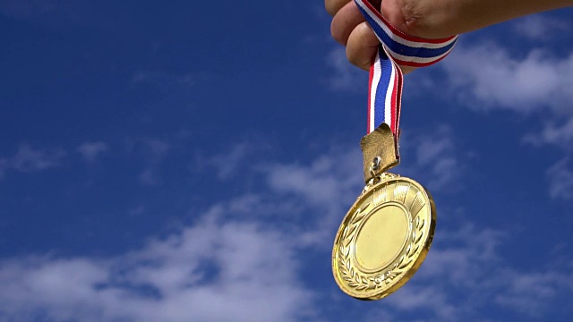 优胜奖概念:商人双手举着带着丝带的金牌，蓝天背景下展示体育或商业上的成功，慢动作视频视频素材