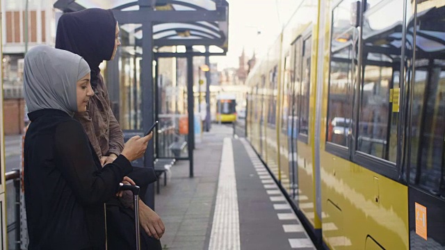 两个女性穆斯林朋友在智能手机上看交通时刻表(慢镜头)视频素材