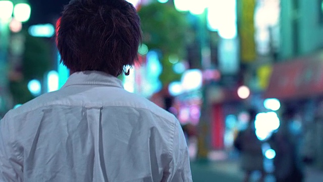 下面是日本年轻人在晚上穿过大城市的街道穿白衬衫。在大城市广告广告牌的背景下，灯光在夜晚闪烁。视频下载