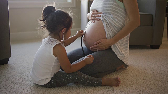 年轻的女孩听着她妈妈怀孕的肚子视频素材