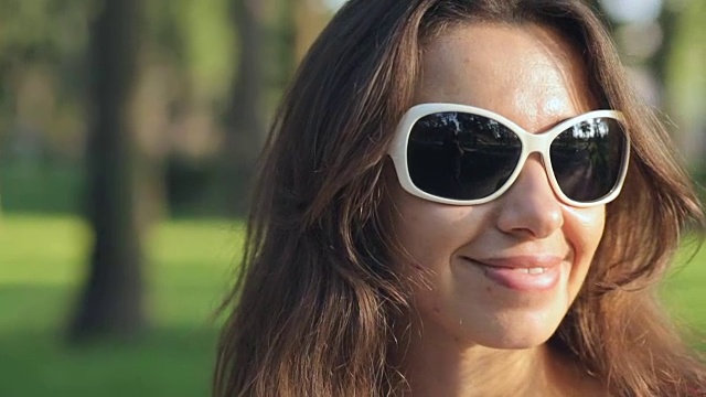 夏日公园里戴着墨镜的快乐年轻女子视频下载