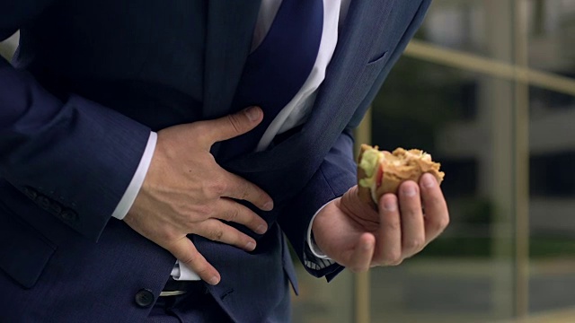 办公室职员在吃不健康的汉堡包时感到腹部不适视频下载
