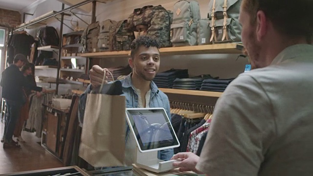 在现代化的市中心服装店，年轻的顾客在平板电脑上完成交易，与收银员握手。视频素材