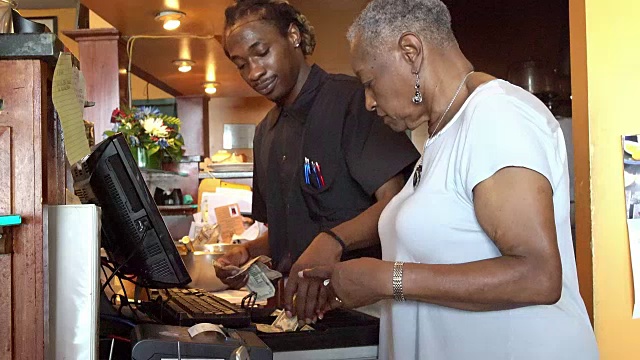 在当地一家小餐馆里，一位活跃的77岁黑人女商人和酒保一起在收银机上数钱视频下载