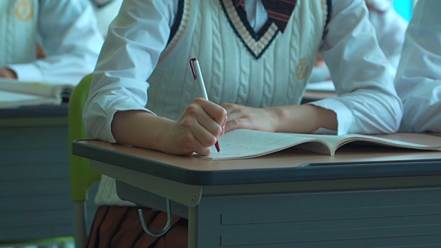 一个女学生坐在教室里的课本上写字视频下载