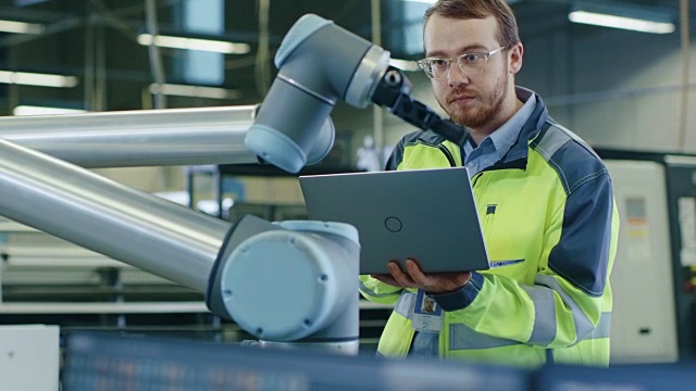在工厂:自动化工程师使用笔记本电脑为机械臂编程。自动化制造业的新时代。视频素材