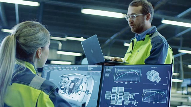 在工厂:男性和女性机械工程师在谈话时使用笔记本电脑和个人电脑。屏幕显示3D引擎概念与CAD软件。视频素材