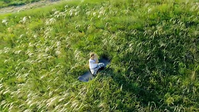 女孩坐在美丽的绿色草地上沉思视频素材