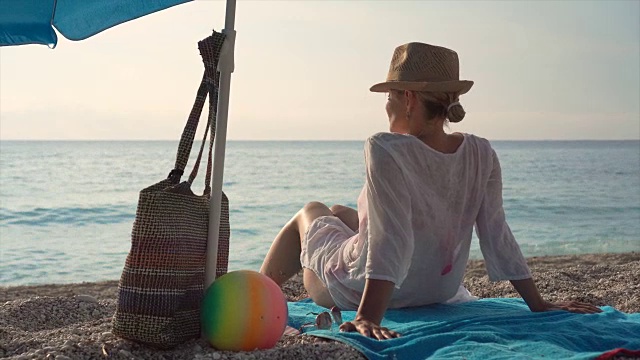 美丽的年轻女子坐在沙滩上晒太阳。视频素材