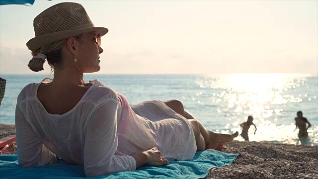 美丽的年轻女子坐在沙滩上晒太阳。视频素材