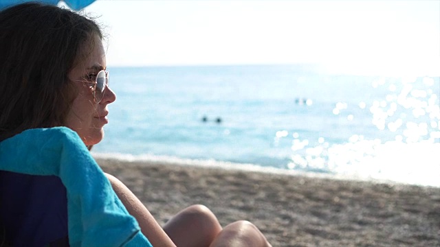 美丽的年轻女孩坐在沙滩上的椅子上晒太阳。视频素材