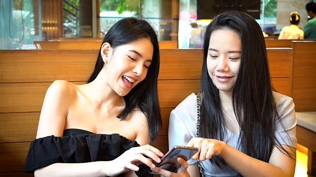 两个亚洲女性朋友用手机一起笑。在日本餐厅享受美好时光的女人视频素材