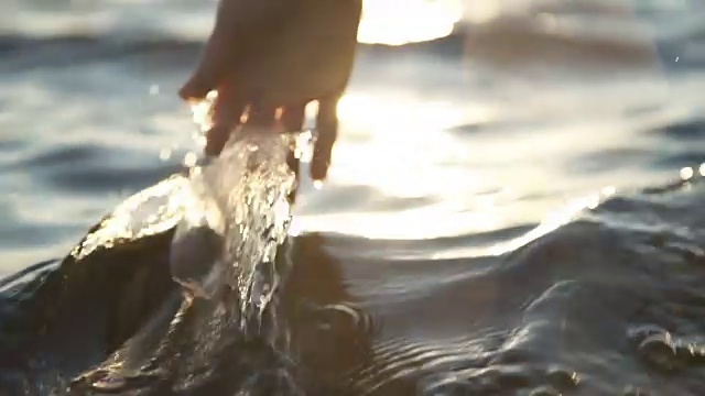 在日落，特写一个女孩的手通过水视频下载