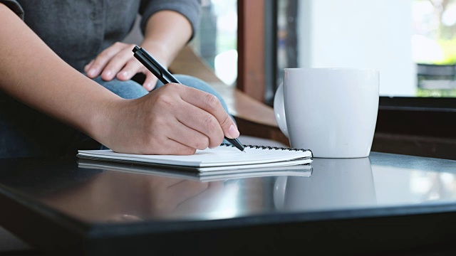 一个女人的手正在桌上一个白纸本上写着什么视频素材