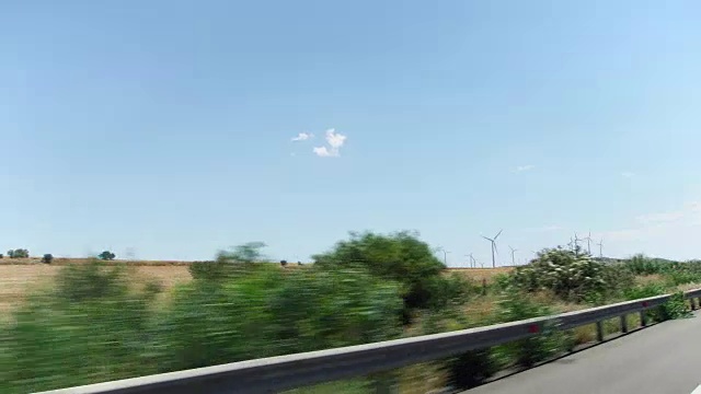 在塞浦路斯的拉纳卡，POV开车从车窗经过田野，树木和风车视频素材
