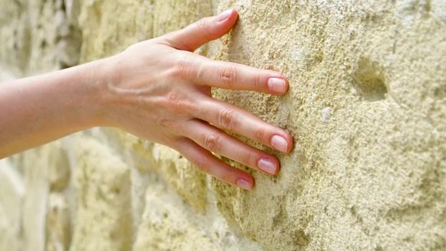 一个女人的手缓慢地靠在古老的石墙上。女性的手触摸岩石的粗糙表面视频素材