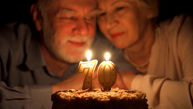 相爱的老年夫妇晚上在家用蛋糕庆祝结婚纪念日。吹灭蜡烛视频下载