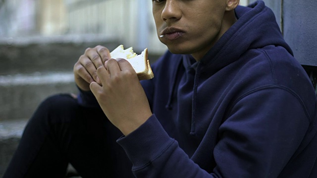 饥饿的美国黑人少年急切地吃着三明治，贫穷的家庭，危机视频素材