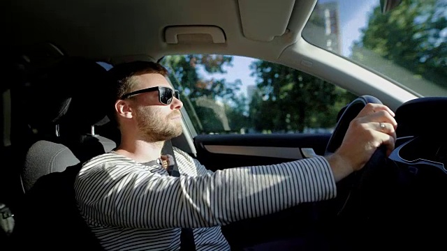 一个时尚的男人在夏天开着一辆车在城市里的侧视图视频素材