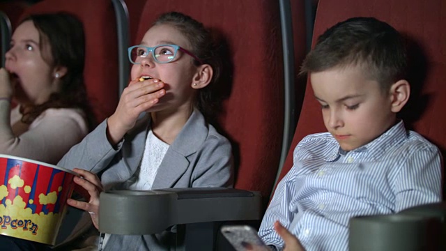 小女孩在电影院吃爆米花。男孩在电影院用智能手机视频素材