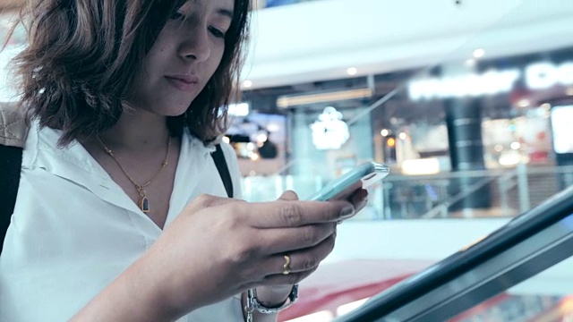 美丽的年轻女子迷人的近距离在商场扶梯上使用移动智能手机在购物中心视频素材