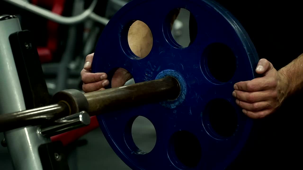 多民族男子将金属圆盘放在运动弹丸上进行力量训练的特写。视频下载