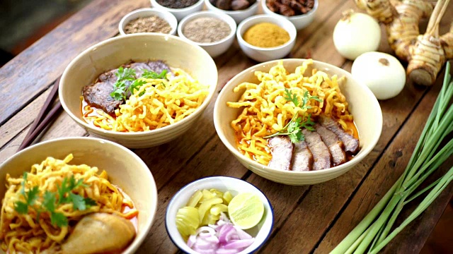 抬高镜头:Khao Soi食谱，木桌上放着泰国北部风味的咖喱面汤，里面有香草和香料。视频下载