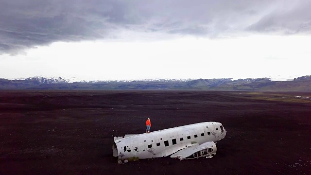 一名年轻女子站在坠毁在黑沙滩上的飞机上，环顾四周，思考周围的环境。这是冰岛著名的旅游景点，并与残骸合影——4K分辨率视频素材