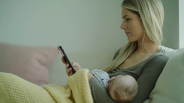多任务母亲坐在沙发上护理婴儿儿子和手机短信的特写/ Lehi，犹他州，美国视频下载