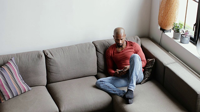 年轻的成年男性在沙发上使用智能手机视频素材