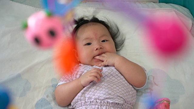 婴儿亚洲女孩在婴儿床看移动玩具。视频素材