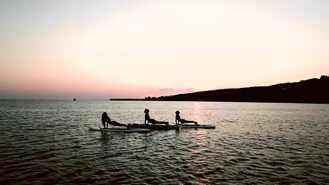 日落时分，年轻女子在海上练习瑜伽的剪影视频素材
