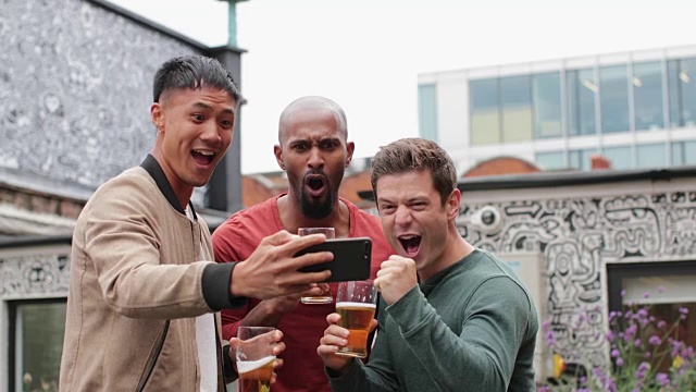 男性朋友在户外酒吧用智能手机看体育比赛视频素材