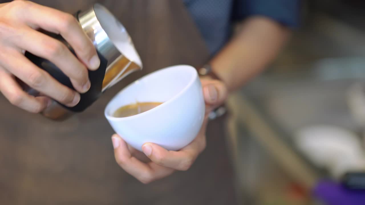 咖啡师把拿铁艺术放进咖啡杯里。视频素材