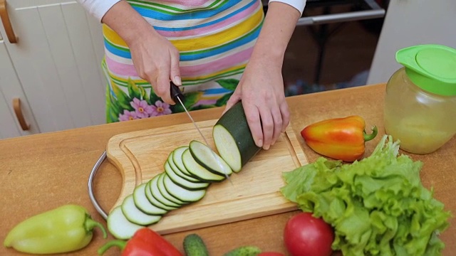 妇女的手家庭主妇用刀在厨房桌上的砧板上切新鲜的西葫芦视频素材
