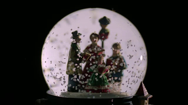把焦点放在一个雪球里的一组塑料颂歌歌手的前景上的一个孩子。视频下载