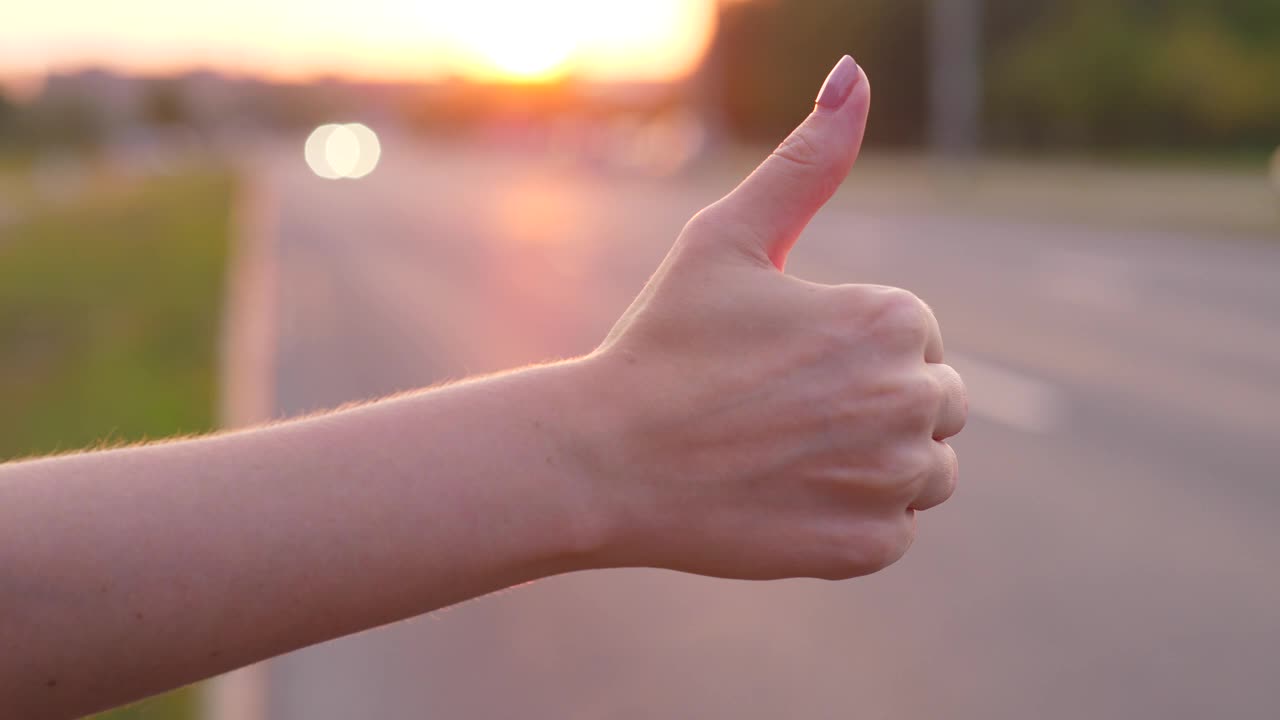 女人手抓车在路上，竖起大拇指，搭便车的概念视频下载
