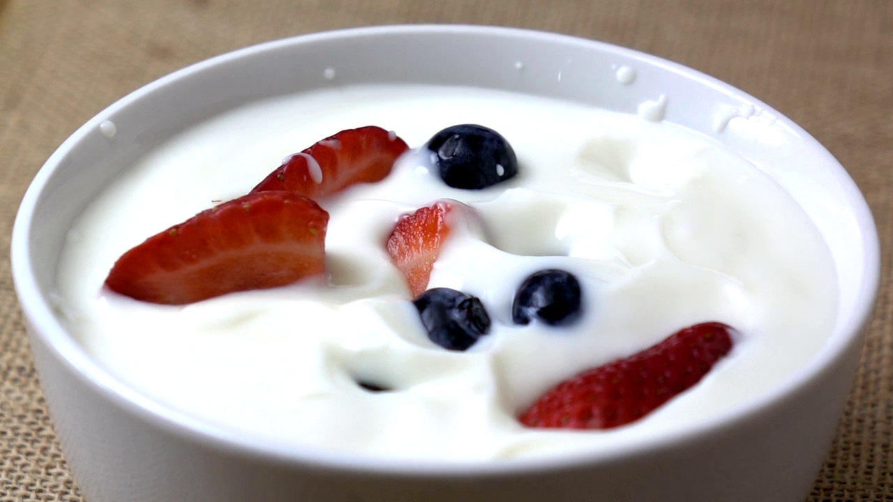 草莓和蓝莓掉进酸奶里的慢动作。早上的早餐。视频素材
