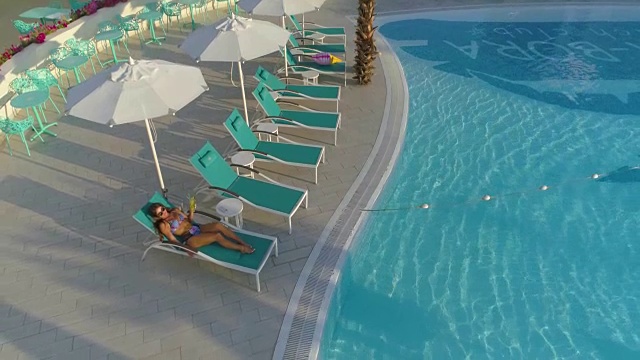 美丽的女孩躺在游泳池旁的躺椅上。视频下载