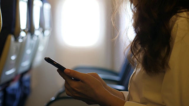 年轻女子在飞机上使用智能手机视频下载