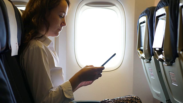 商务女性在飞机上用智能手机发短信视频下载