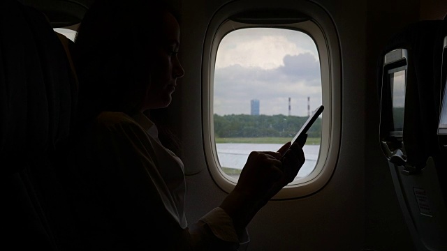 一个女人在飞机上拿着智能手机，靠着窗户聊天视频下载