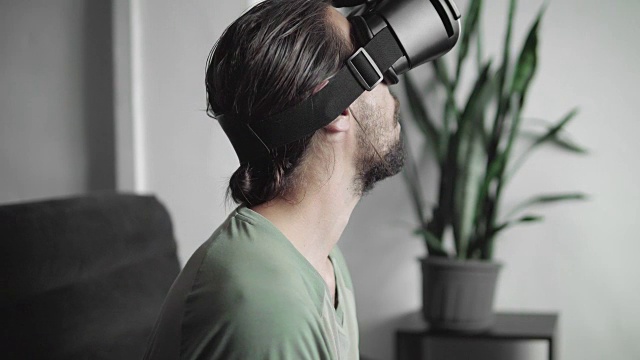 年轻的大胡子嬉皮士开始使用他的VR头盔显示器与耳机进行虚拟现实游戏或观看360视频，迷住和惊讶的东西。视频素材
